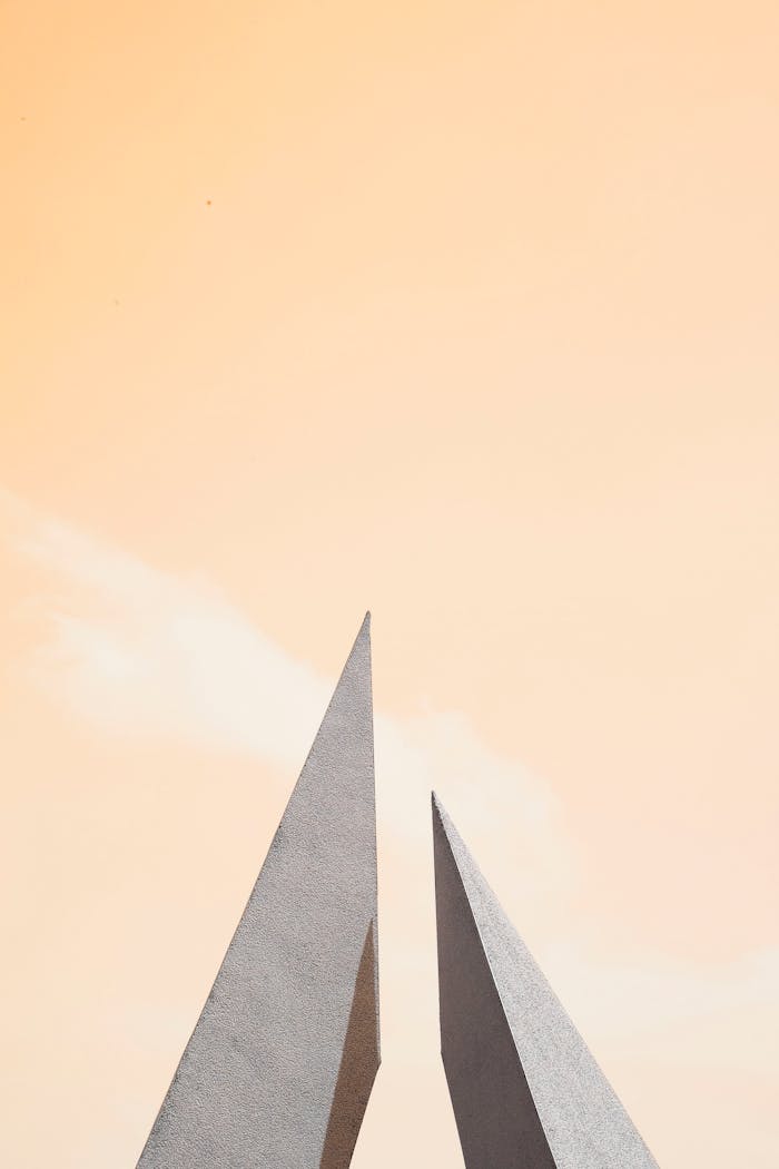 our-services-2 Modern minimalist architecture featuring sharp geometric forms against a soft pastel sky.