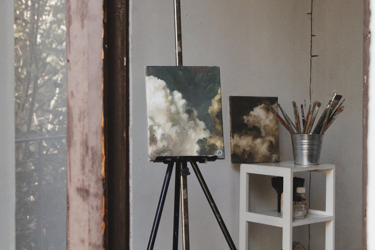 about-01 Cozy art studio featuring cloud paintings on easels and paintbrushes, captured indoors.